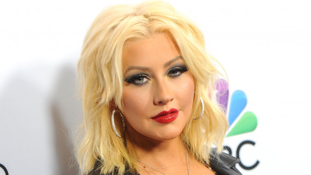 Christina Aguilera in a black leather jacket and silver hoop earrings, looking at the camera with a serious expression