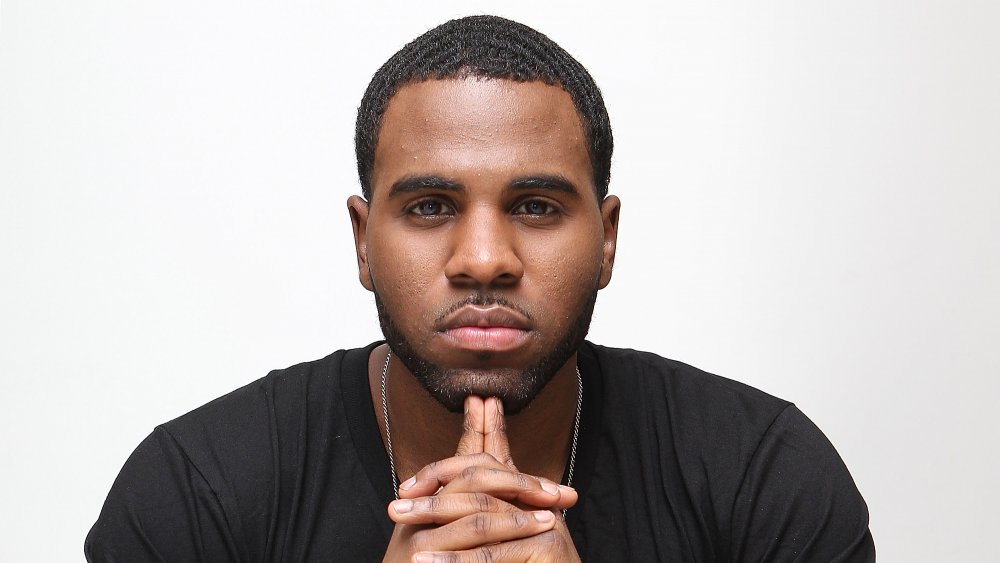 Jason Derulo in a black t-shirt and silver chain, posing with a neutral expression