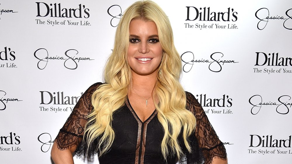 Jessica Simpson in a black lace top, smiling with her hands on her hips