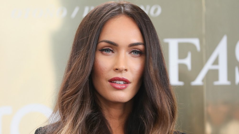 Megan Fox in a black suit, posing with wavy hair and a neutral expression