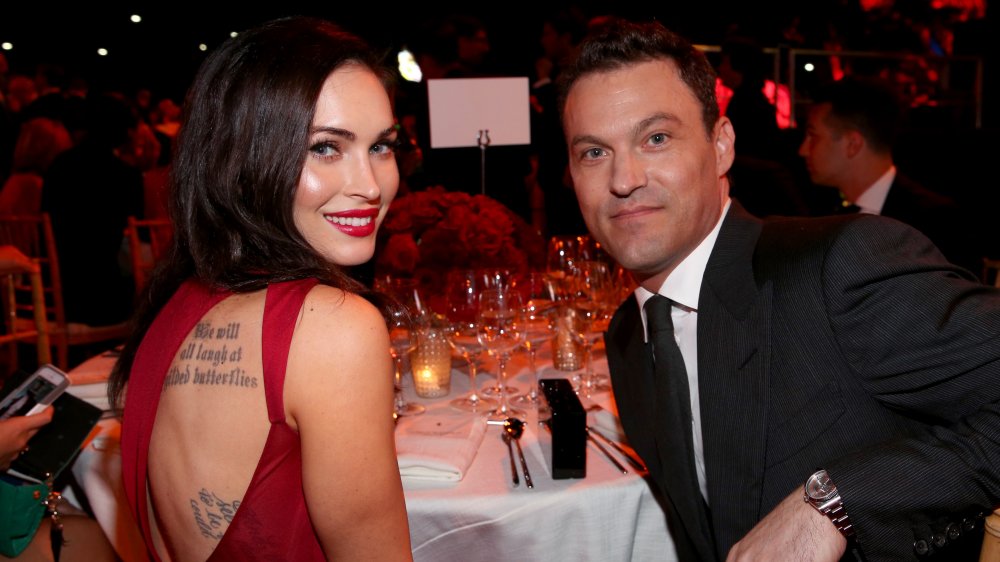 Megan Fox in a red dress and Brian Austin Green in a black suit, sitting at a dinner event together