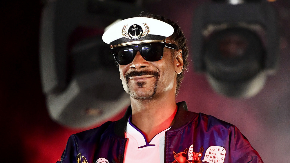 Snoop Dogg smiling onstage wearing aviator sunglasses and a visor