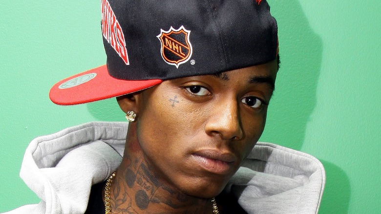 Soulja Boy posing in front of a green wall