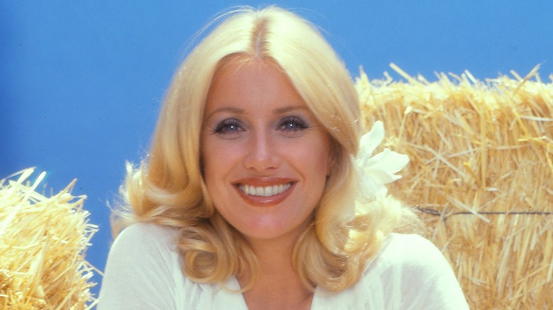 Suzanne Somers smiling and posing in sparkly gold top and hairbow