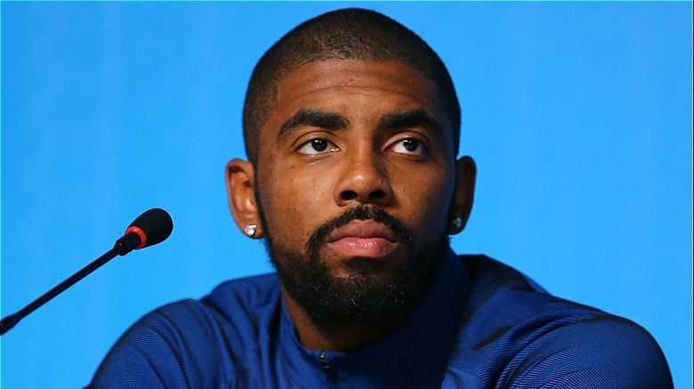 Kyrie Irving sits at a microphone in front of a blue background