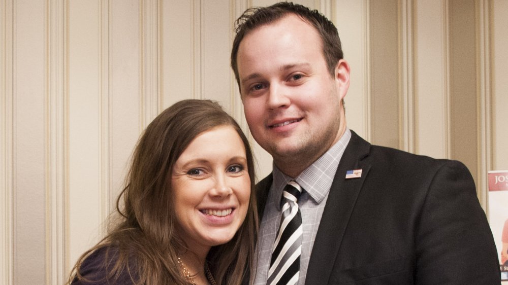 Anna Duggar in a purple dress, smiling and holding her baby bump, and Josh Duggar smiling in a black suit