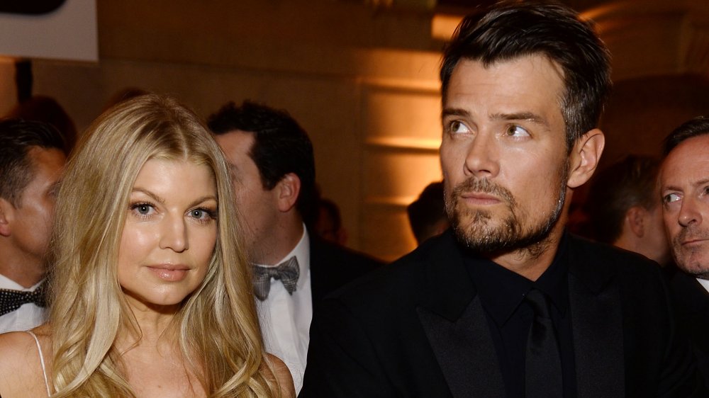 Fergie in a white dress, Josh Duhamel in a black suit, both with serious expressions