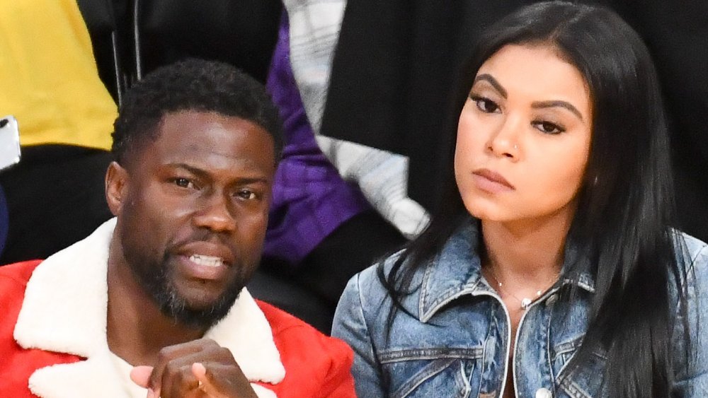 Kevin Hart in a red jacket, Eniko Parrish in a jean jacket, both with serious expressions