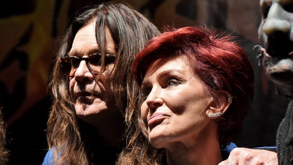 Ozzy Osbourne with his arm around Sharon Osbourne, both with neutral expressions