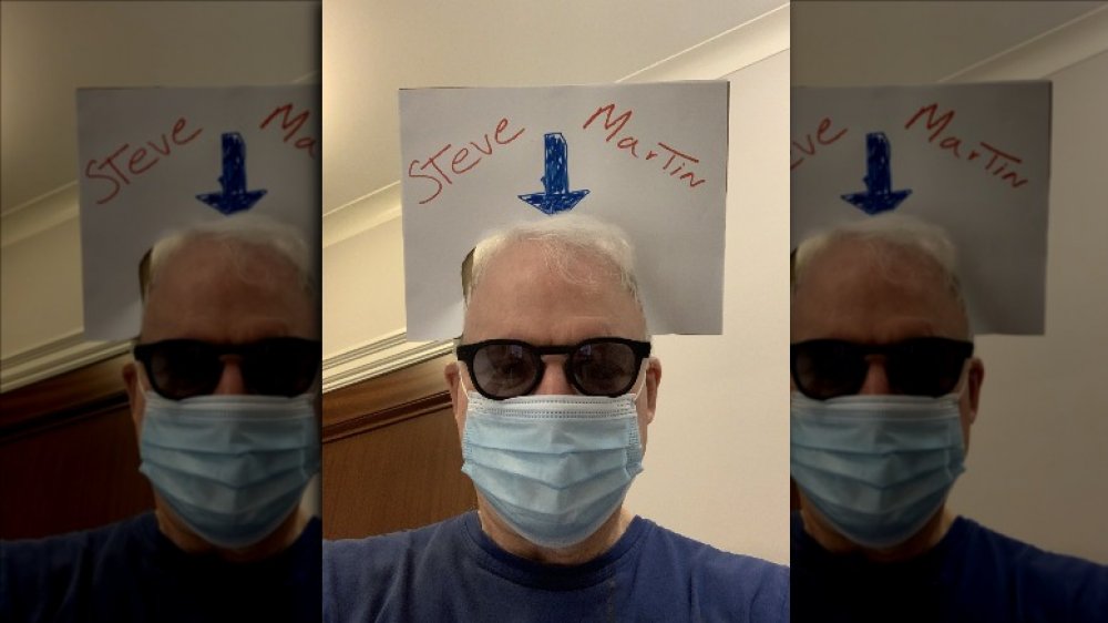 Steve Martin in his mask with a sign on his head