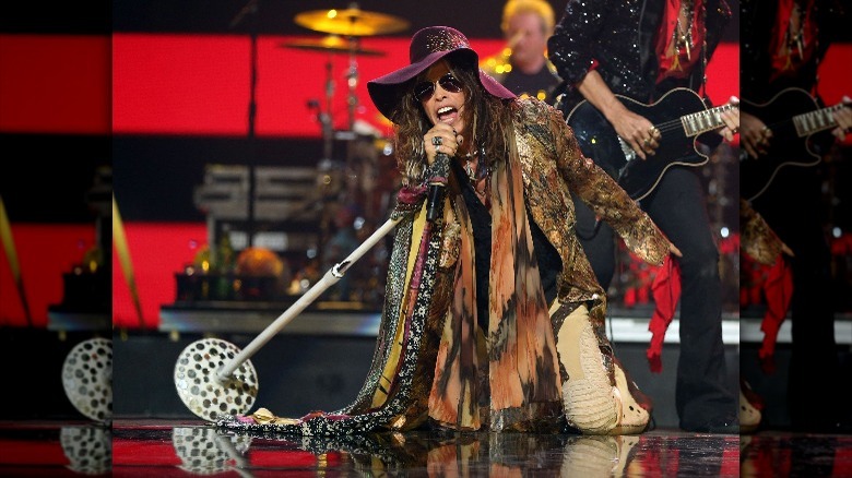 Steven Tyler performing in a purple hat and a lot of scarves
