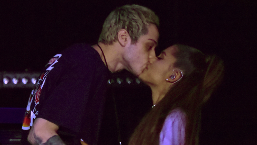 Pete Davidson and Ariana Grande kissing on stage. 