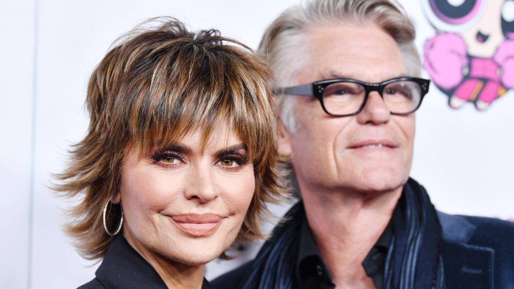 Lisa Rinna looking at the camera, and Harry Hamlin in the background looking off to the side, while attending a fashion show in 2020