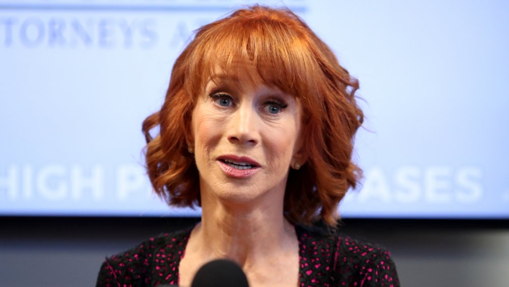Kathy Griffin in a black and pink dress, speaking tearfully into a mic