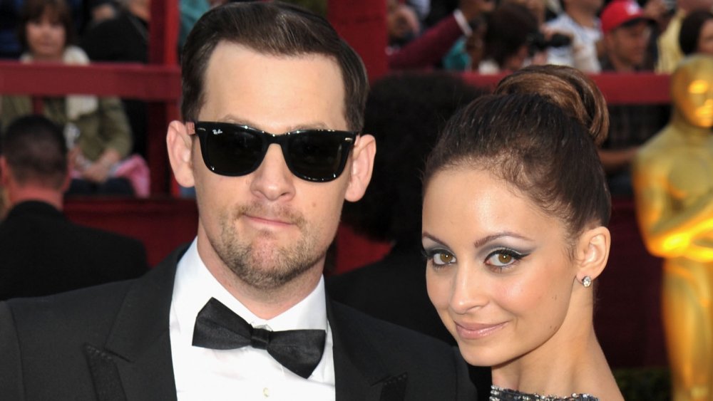 Joel Madden in a black tux and sunglasses, Nicole Richie in a silver dress smirking at the 2010 Oscars