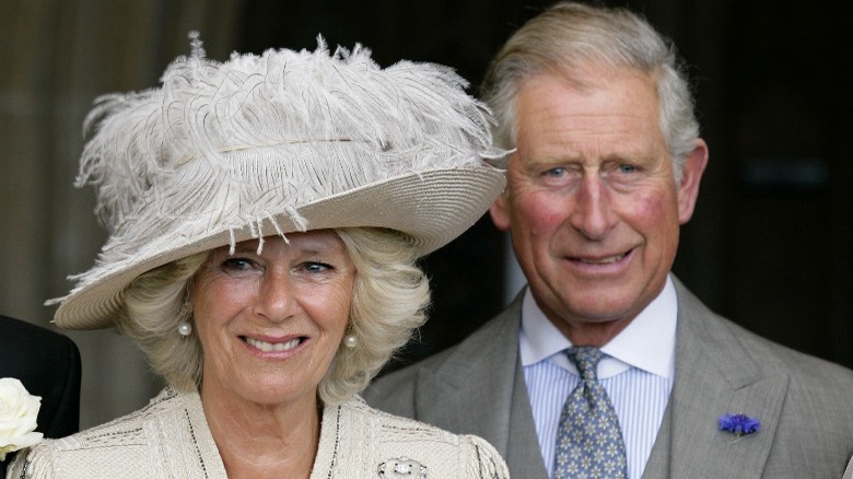 Camilla Parker Bowles in a hat with Prince Charles standing behind her