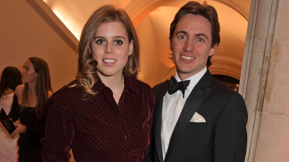 Princess Beatrice in a maroon outfit, Edoardo Mapelli Mozzi in a black tux, both smiling at an event