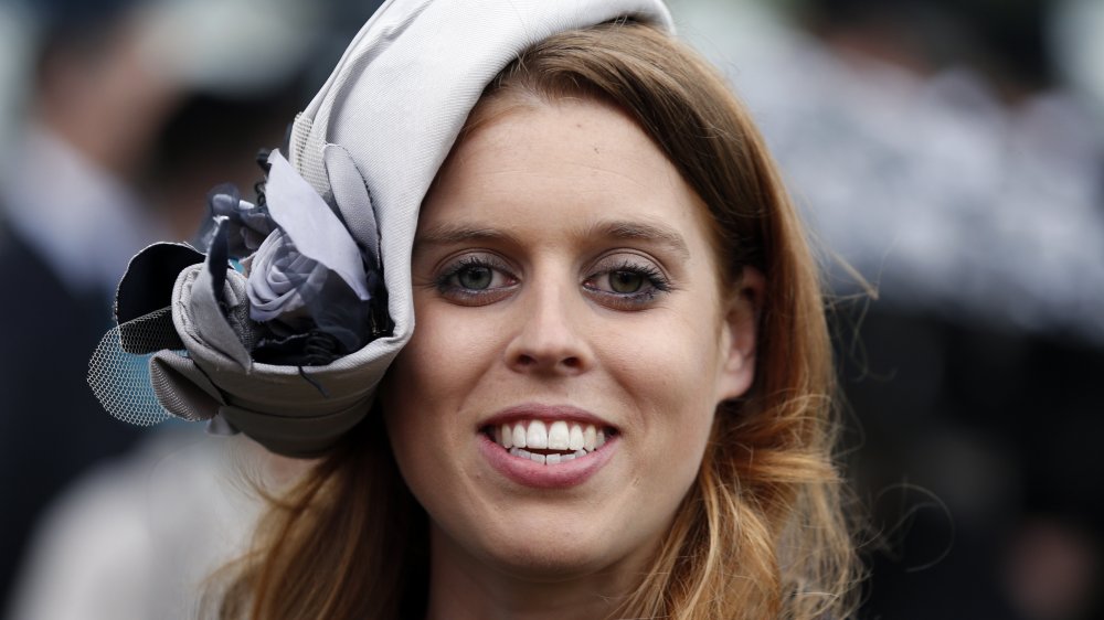 Princess Beatrice smiling big while wearing a light purple hat, staring straight at the camera