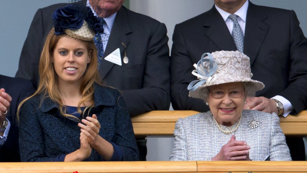 Princess Beatrice in a dark blue outfit and hat, Queen Elizabeth in a light blue outfit, both clapping and smiling