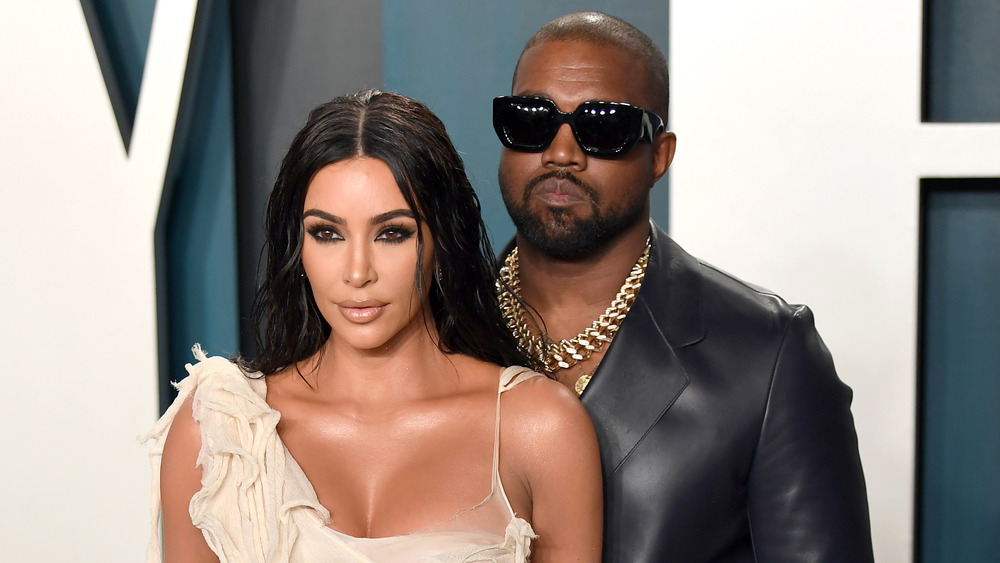 Kim Kardashian with Kanye West in sunglasses behind her posing together