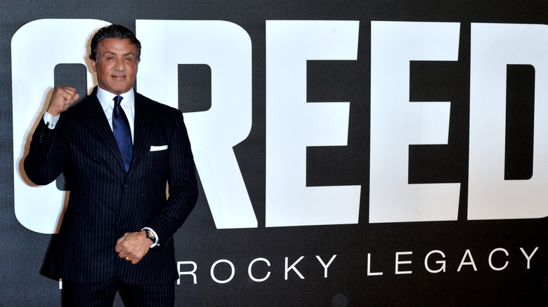 Sylvester Stallone posing in front of Creed sign