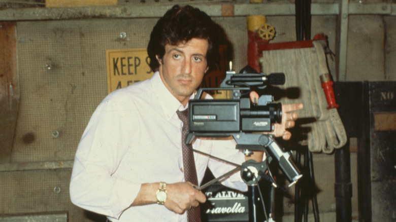 Sylvester Stallone looking off camera while operating a film camera