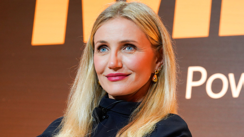 Cameron Diaz smiling with a bold pink lipstick and gold earrings