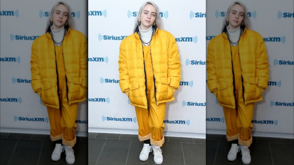 Billie Eilish in a puffy yellow jacket with matching rolled-up pants and white shoes