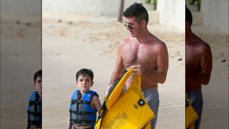 Eric and Simon Cowell walking on beach wearing life jackets