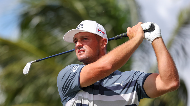 Bryson DeChambeau swings club in a white hat