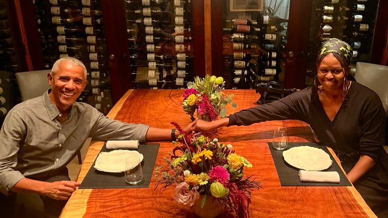 Barack Obama and Michelle Obama holding hands across a large dinner table