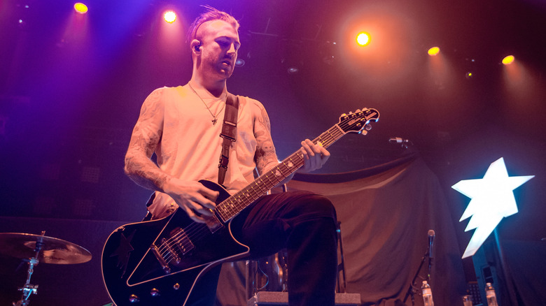 Jordan McGraw with a mohawk wearing a white tank top and playing a guitar