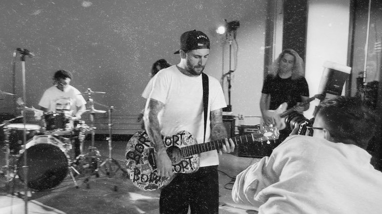 Black and white photo of Jordan McGraw wearing a backwards ball cap, white t-shirt, and jeans while playing guitar