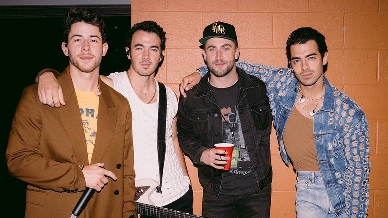 Nick Jonas, Kevin Jonas, Jordan McGraw, and Joe Jonas wearing stage clothes posing backstage