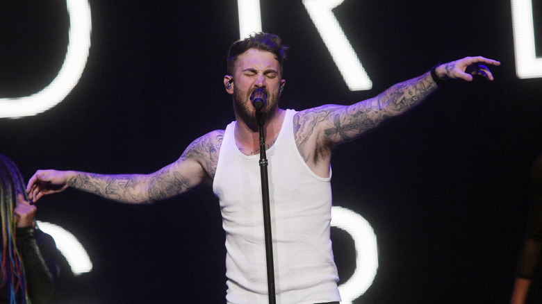 Jordan McGraw wearing a white tank top singing into a microphone with his eyes closed