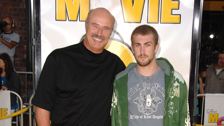 Dr. Phil McGraw wearing a black collared shirt and Jordan McGraw wearing a graphic t-shirt and green hoodie