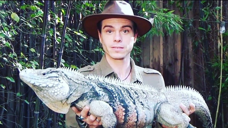 Matthew Lawrence, wearing a white t-shirt, backward hat, glasses, holding a reptile