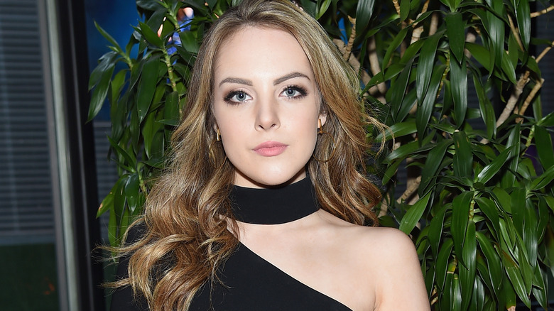 Liz Gillies with long wavy dirty blonde hair and a black top with choker