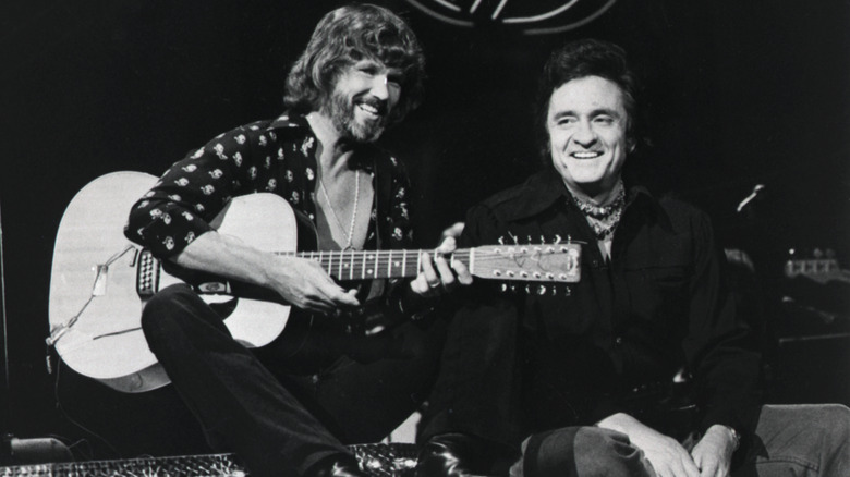 Kris Kristofferson and Johnny Cash smiling together, Kristofferson holding a guitar