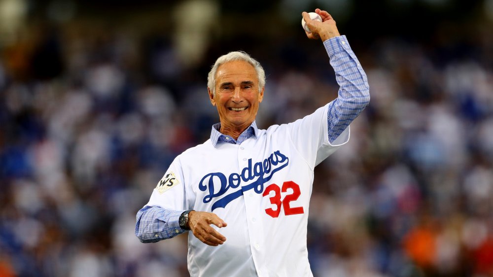 An older Sandy Koufax smiling while throwing a pitch