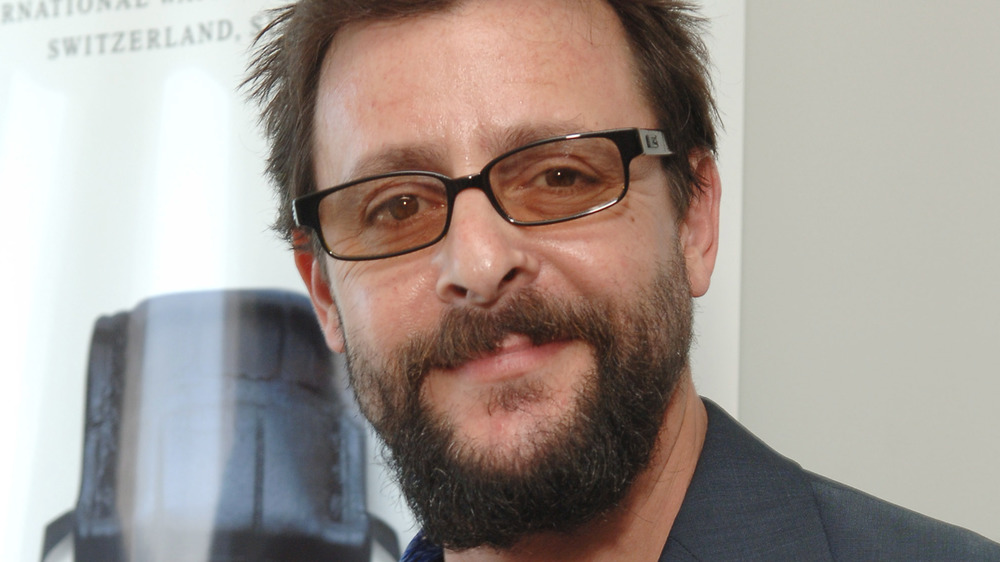 Judd Nelson smirking, wearing glasses, a beard, and short hair