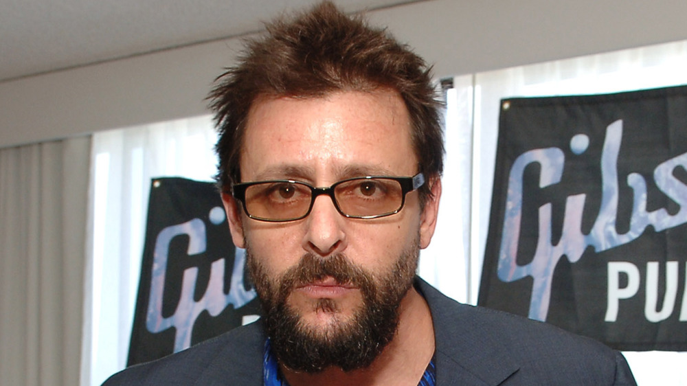 A bearded Judd Nelson in tinted glasses 