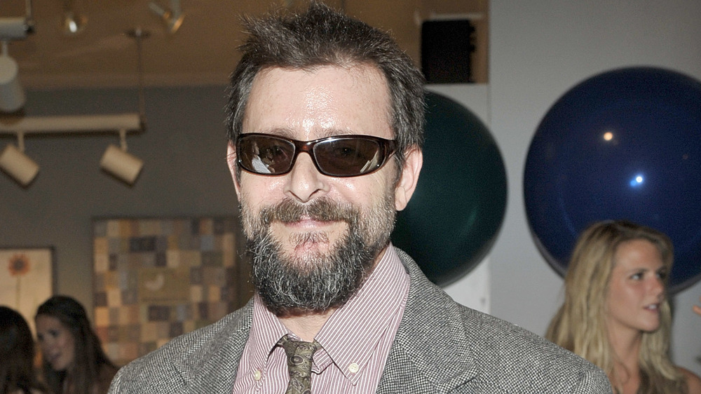 A bearded Judd Nelson smirking and wearing sunglasses 