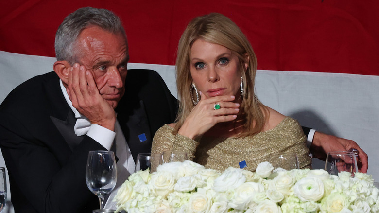 RFK Jr. and Cheryl Hines at the Alfred E. Smith Foundation Dinner, seated and both touching their faces