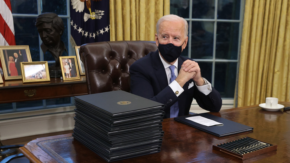 Photos of the Biden family are arranged on a desk behind Joe Biden preparing to sign orders