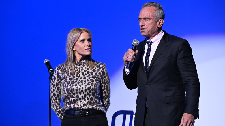 Cheryl Hines standing next to RFK Jr. as he speaks on stage