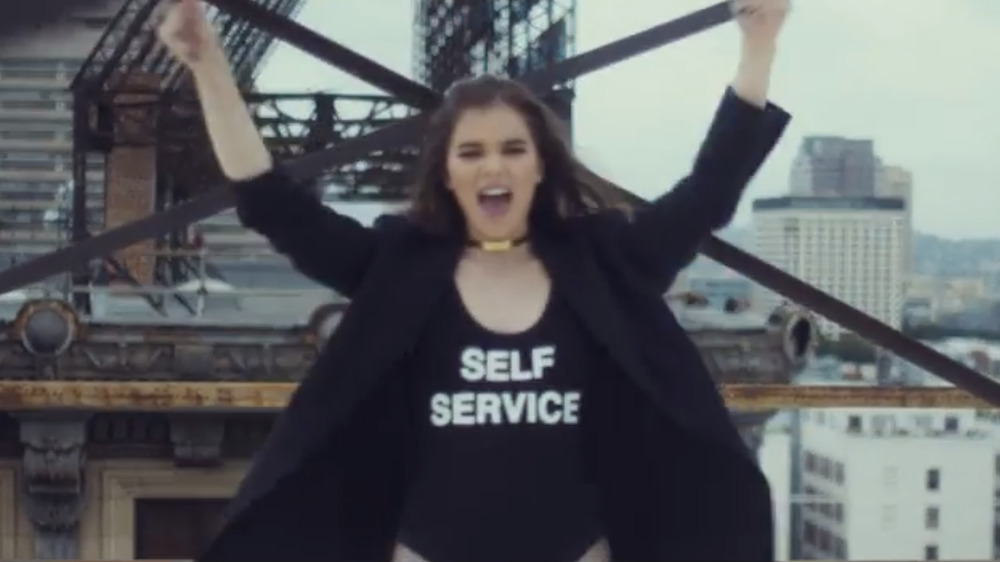 Hailee Steinfeld wearing a shirt that reads "Self Service" in her music video