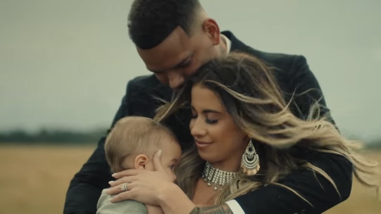 Kane Brown hugging his wife Katelyn Jae, and their daughter Kingsley, screenshot from "Worship You" music video, Katelyn smiling, in a field