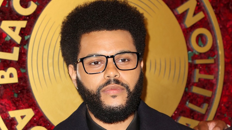 The Weeknd wears black rimmed glasses while posing for a photo