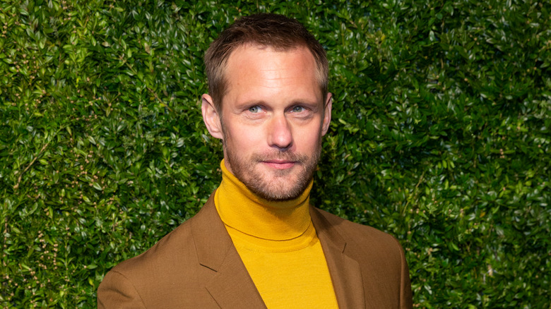 Alexander Skarsgård poses in yellow turtleneck and brown suit